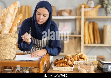 Europäische Frau im Hijab, die Papierkram während der Bäckerei überprüft Stockfoto