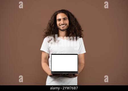 Selbstbewusster junger Mann mit lockigen Haaren posiert mit einem Laptop Stockfoto