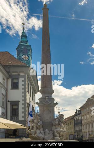 Ljubljana, Slowenien - 28. Juni 2024: Robbov vodnjak oder Robba-Brunnen, hoher Betonobelisk mit Statuen unter blauer Wolkenlandschaft. Uhrenturm der Stadt h Stockfoto