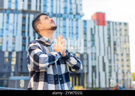 Reifer kaukasischer Mann männliches Gesicht, das in der Innenstadt steht und Palmen faltet und Gott um Hilfe bittet. Ängstliches Konzept. Ein Mann mittleren Alters denkt stiller Bruch, der gegen das Gebäude steht. Stockfoto