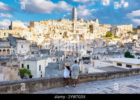 Ein Paar steht Hand in Hand und bestaunt die atemberaubende Landschaft von Matera in Apulien, Italien, wo antike Steinbauten majestätisch gegen einen dramatischen Himmel ragen. Mann und Frau auf einer Städtereise Stockfoto