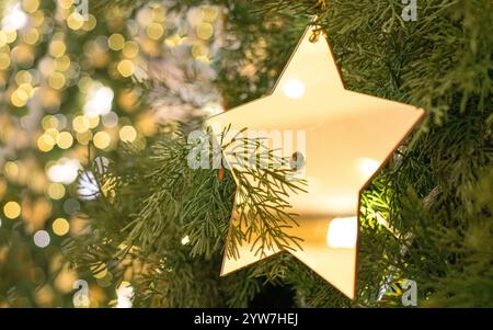 Weihnachtsdekoration eines goldenen Sterns, der auf einem Baum hängt, mit hellem Bokeh-Hintergrund. Stockfoto