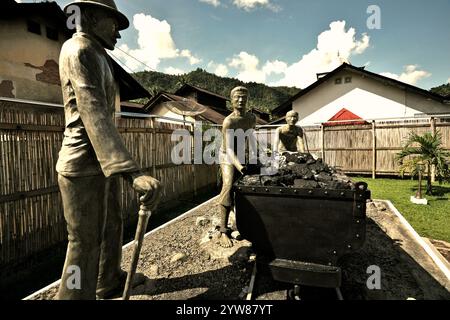 Skulpturen, die einen Aufseher zeigen, der Arbeiter beim Transport von Kohle mit einem Eisenbahnwagen in Sawahlunto, einer ehemaligen Kohlebergbaustadt in Sumatra, aufmerksam macht. Stockfoto