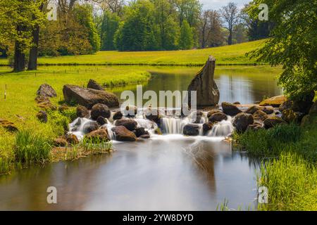 Ruhiger Fluss mit kaskadierendem Wasser über Felsen in einer üppigen grünen Landschaft Stockfoto