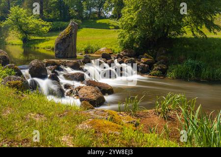 Ruhiger Fluss mit kaskadierendem Wasser über Felsen in einer üppigen grünen Landschaft Stockfoto