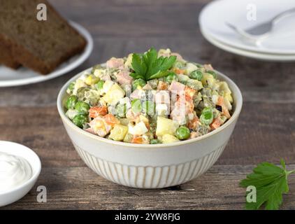Russischer traditioneller Wintersalat Olivier aus Eiern, Gemüse, Wurst, Erbsen auf hölzernem Hintergrund. Russische Küche Stockfoto