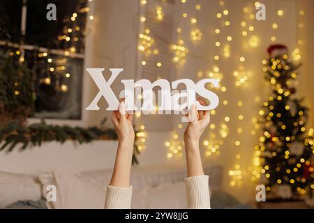 Frau, die WEIHNACHTSSCHILD mit weihnachtsbeleuchtung in ihrem Haus hält, gemütliche weihnachten Stockfoto