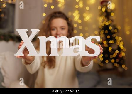 Eine Person mit einem weißen Weihnachtsschild mit einem verschwommenen Weihnachtsbaum und Lichtern im Hintergrund. Stockfoto
