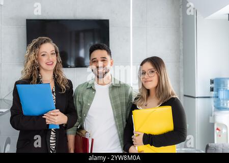 Drei lächelnde Geschäftsleute halten Mappen in der Hand, die Teamarbeit und Zusammenarbeit in einem modernen Bürobereich zeigen Stockfoto
