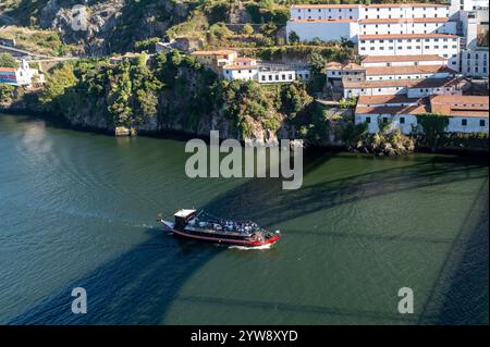Porto, Portugal - 12. September 2024 : Ein Boot fährt in ruhigen Gewässern in der Nähe von bezaubernden Dörfern am Hügel unter klarem Himmel. Stockfoto
