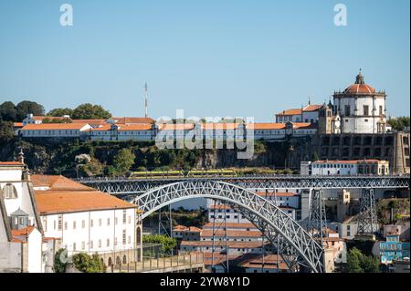 Porto, Portugal - 13. September 2024 : Ein Zug fährt über die berühmte Brücke mit farbenfrohen Gebäuden im Hintergrund. Stockfoto