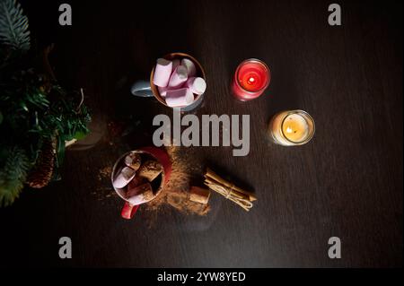 Eine gemütliche Winterszene mit heißem Kakao mit Marshmallows, umgeben von brennenden Kerzen und festlichem Grün auf einem dunklen Holztisch, schafft Stockfoto