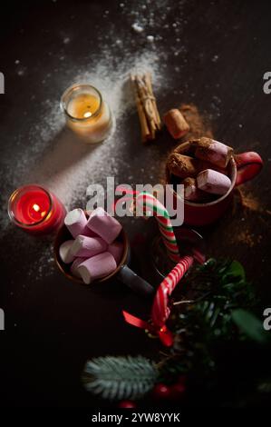 Gemütliche heiße Schokoladenszene mit Marshmallows, Zuckerstangen und Weihnachtskerzen auf dunklem Hintergrund. Stockfoto