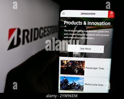 In dieser Abbildung hält eine Person ein Smartphone mit der Webseite des japanischen Reifenunternehmens Bridgestone Corporation vor dem Logo. Stockfoto