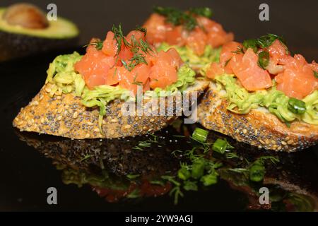 Vollkornbruschetta garniert mit pürierter Avocado, frischem Lachs und aromatischen Kräutern für eine geschmackvolle Vorspeise Stockfoto