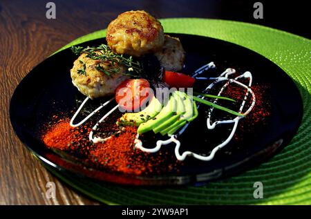 Hühnchenkoteletts mit Avocado und Tomaten auf einem schwarzen Teller Stockfoto