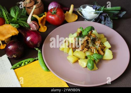 Köstliche Bratkartoffeln mit Pfifferlingen und Kräutern serviert auf einem Teller mit Sauerrahm, umgeben von frischem Gemüse Stockfoto