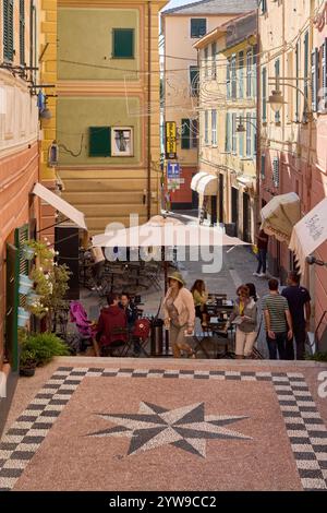 Savona. Italia - 10. Dezember 2024: Eine lebhafte Straße mit farbenfrohen Gebäuden, grünen Fensterläden und einem Café im Freien fängt die lebhafte Atmosphäre am Meer ein Stockfoto