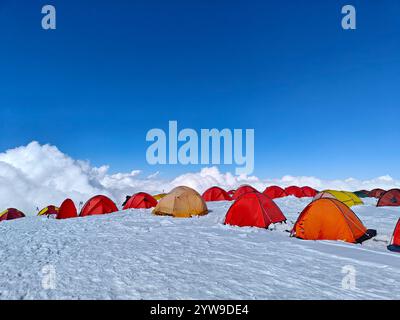 Bunte Zelte stehen auf einem verschneiten Berggipfel unter einem leuchtend blauen Himmel und laden Abenteuerlustige ein. Stockfoto