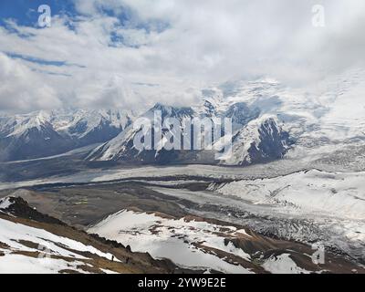 Majestätische Gipfel erheben sich über einem riesigen Gletscher, umgeben von felsigem Gelände und dramatischen Wolken, die die Schönheit der Natur enthüllen. Stockfoto