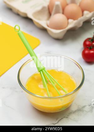 Geschlagene Eier und Schneebesen in Glasplatte auf dem Tisch. Stockfoto