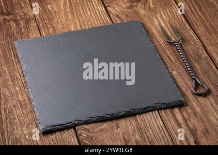 Schwarzer Steinschieferständer und Fleischgabel auf einem Holztisch, Lebensmittelhintergrund, Vorlage für Designer Stockfoto