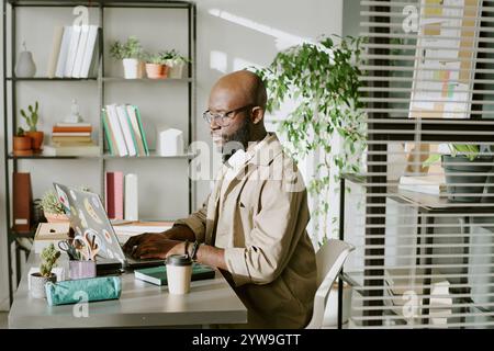Seriöser afroamerikanischer Büroangestellter sitzt am Schreibtisch und programmiert im biophilen Büro des IT-Unternehmens Stockfoto
