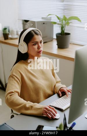 Hochwinkelaufnahme einer jungen, brünetten Programmiererin, die Musik programmiert und hört, konzentrierte sich auf die Arbeit Stockfoto