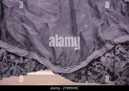 Ungewöhnliche Stoffe, zerknitterte dünne dunkelblaue Baumwolle, Viskose mit schöner Spitze mit Blumen befindet sich auf einem weißen Kunststoffhintergrund. Stockfoto