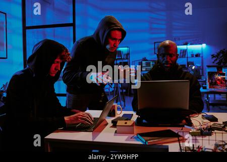 Birassische Hacker in schwarzen Hoodies diskutieren Programmdetails im Büro Stockfoto