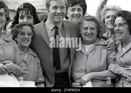 1968, historisch, du lachst Weibliche Catering-Mitarbeiter, die miteinander lachen, während sie für ein Foto mit dem beliebten TV-Moderator und Radio-DJ David „Diddy“ Hamilton auf einem Freiluftfest in Burnley, Lancs, England, Großbritannien stehen. Hamilton wurde vom Komiker Ken Dodd als „Diddy“ bezeichnet, da Hamilton 1959 mit der Ausstrahlung begann und 2021 noch im Radio war. Stockfoto