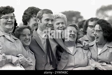 1968, historisch, du lachst Weibliche Catering-Mitarbeiter, die miteinander lachen, während sie für ein Foto mit dem beliebten TV-Moderator und Radio-DJ David „Diddy“ Hamilton auf einem Freiluftfest in Burnley, Lancs, England, Großbritannien stehen. Hamilton begann seine Ausstrahlung 1959 und war 2021 noch im Radio. Stockfoto