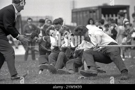 1968, historisch, draußen auf einem Feld auf einem Stadtfest, männliche Konkurrenten in Hemden, Hosen und Kochstiefeln, die an einem Tauziehen teilnehmen, während ihr Trainer neben ihnen ermutigt, England, Großbritannien. Stockfoto