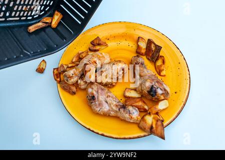 Wie man gekochte Hähnchenschenkel und Kartoffeln auf einem Teller in einer Fritteuse auf einem schönen blauen Tisch umwirft Stockfoto