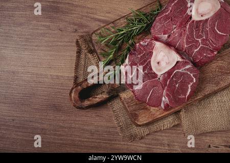 Knöchel auf dem Knochen, rohes Fleisch für Ossobuco, auf einem hölzernen Schneidebrett, mit einem Zweig Rosmarin und Gewürzen, Blick von oben, keine Leute Stockfoto