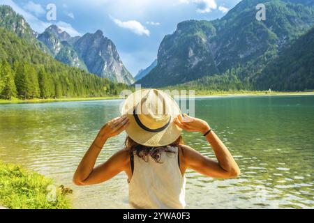 Eine junge Frau mit Strohhut, die die Landschaft des toblacher Sees und der dolomiten während der Sommerferien in italien bewundert Stockfoto