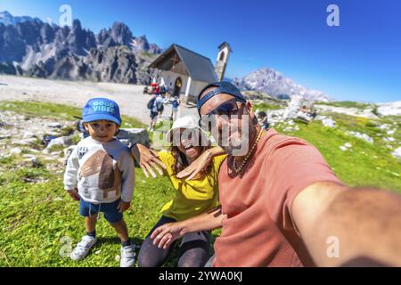 Die Familie macht ein Selfie mit den atemberaubenden Bergen von Tre cime di lavaredo und der Kapelle im Hintergrund und genießt den Sommerurlaub in den dolomiten. Kappe Stockfoto