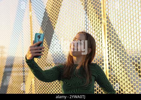 Lächelnde Frau, die Videoanrufe bei Sonnenuntergang macht, auf den Smartphone-Bildschirm schaut und mit Freunden, Familie, Paar... Stockfoto
