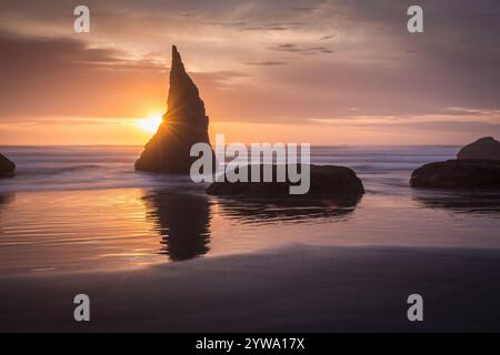 Der Sonnenuntergang am Bandon Beach besticht durch majestätische Meeresstapel, goldene Strahlen, die sich auf nassem Sand spiegeln, und ruhige Meereswellen, die eine atemberaubende und ruhige Atmosphäre schaffen Stockfoto