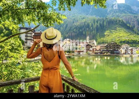 Frau mit Sommerkleidung und Strohhut, die das malerische Dorf alleghe und seinen See in den italienischen dolomiten bewundert Stockfoto