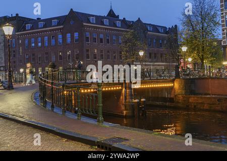 Beleuchtete Brücke über einen Kanal im herbstlichen Abendlicht, Amsterdam, Niederlande Stockfoto