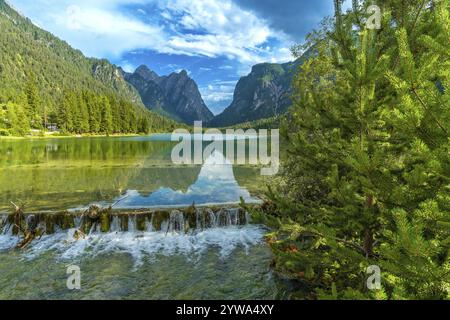 Kristallklares Wasser, das von einem kleinen Wasserfall in den See toblach stürzt und die majestätischen Dolomitgipfel unter einem Sommerhimmel reflektiert Stockfoto