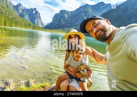 Glückliche Familie, die ein Selfie am transparenten Wasser des toblacher Sees mit den dolomiten im Hintergrund macht und Sommerurlaub genießt Stockfoto