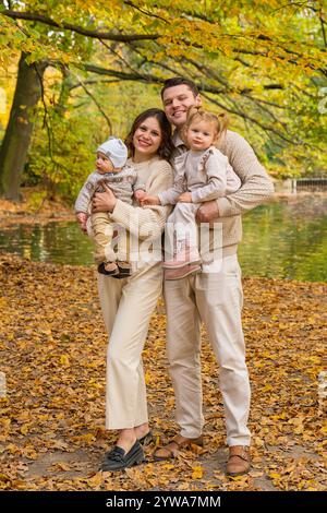 Glückliche junge Familie mit zwei Kindern bei einem Spaziergang im Herbstpark, am Wochenende genießen wir gemeinsame Zeit. Mom hält einen Jungen in den Armen, Dad. Ein Töchter Stockfoto