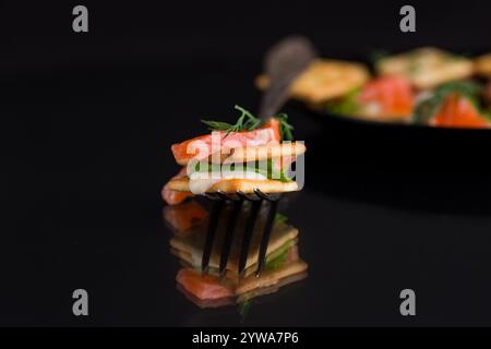Kleine Snack Canapes mit Crackern und leicht gesalzenem rotem Fisch Lachs, isoliert auf schwarzem Hintergrund. Stockfoto