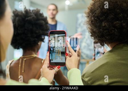 Hände einer jungen Besucherin von Kunstausstellungen oder Auktionen mit Smartphone beim Fotografieren abstrakter Malerei Stockfoto