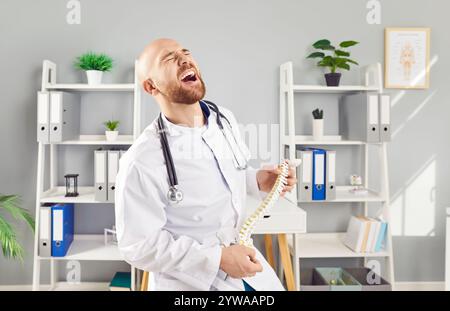 Lustiger junger männlicher Arzt-Orthopäden, der an der Wirbelsäule eines menschlichen Skelett-anatomischen Modells in der Klinik spielt. Stockfoto