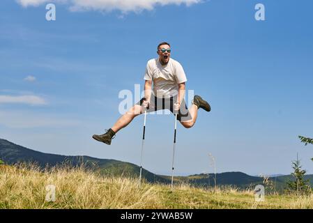 Ein fröhlicher Mann springt bei einer sonnigen Bergwanderung mit Trekkingstöcken hoch in die Luft. Die Szene strahlt Energie, Abenteuer und Liebe für die Natur aus. Stockfoto