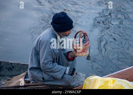 Srinagar, Indien. Dezember 2024. Ein Mann aus Kaschmir bläst Holzkohle, um sie in einem Feuertopf oder Kangri an einem kalten und nebeligen Wintermorgen in Srinagar anzuzünden. Im Kaschmir-Tal herrschte intensive Kälte, da die Mindesttemperatur mehrere Grad unter den Gefrierpunkt fiel. Die Hauptstadt der Region Srinagar verzeichnet die kälteste Nacht der Saison bei minus 5,4 Grad Celsius (41,72 Grad Fahrenheit), berichteten Wetterbeamte in der Himalaya-Region. (Foto: Faisal Bashir/SOPA Images/SIPA USA) Credit: SIPA USA/Alamy Live News Stockfoto