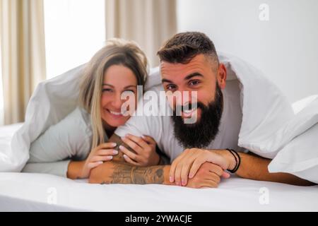 Das junge, glückliche Liebespaar liegt morgens im Bett. Sie haben Spaß und lächeln. Stockfoto